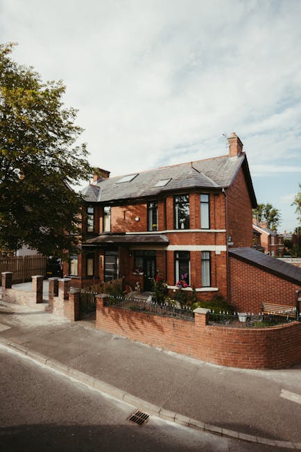 The image shows the front garden area of a traditional two-storey red brick house with a sloped slate roof, located on Blackfen Road. The garden features a small, well-maintained lawn bordered by a lo